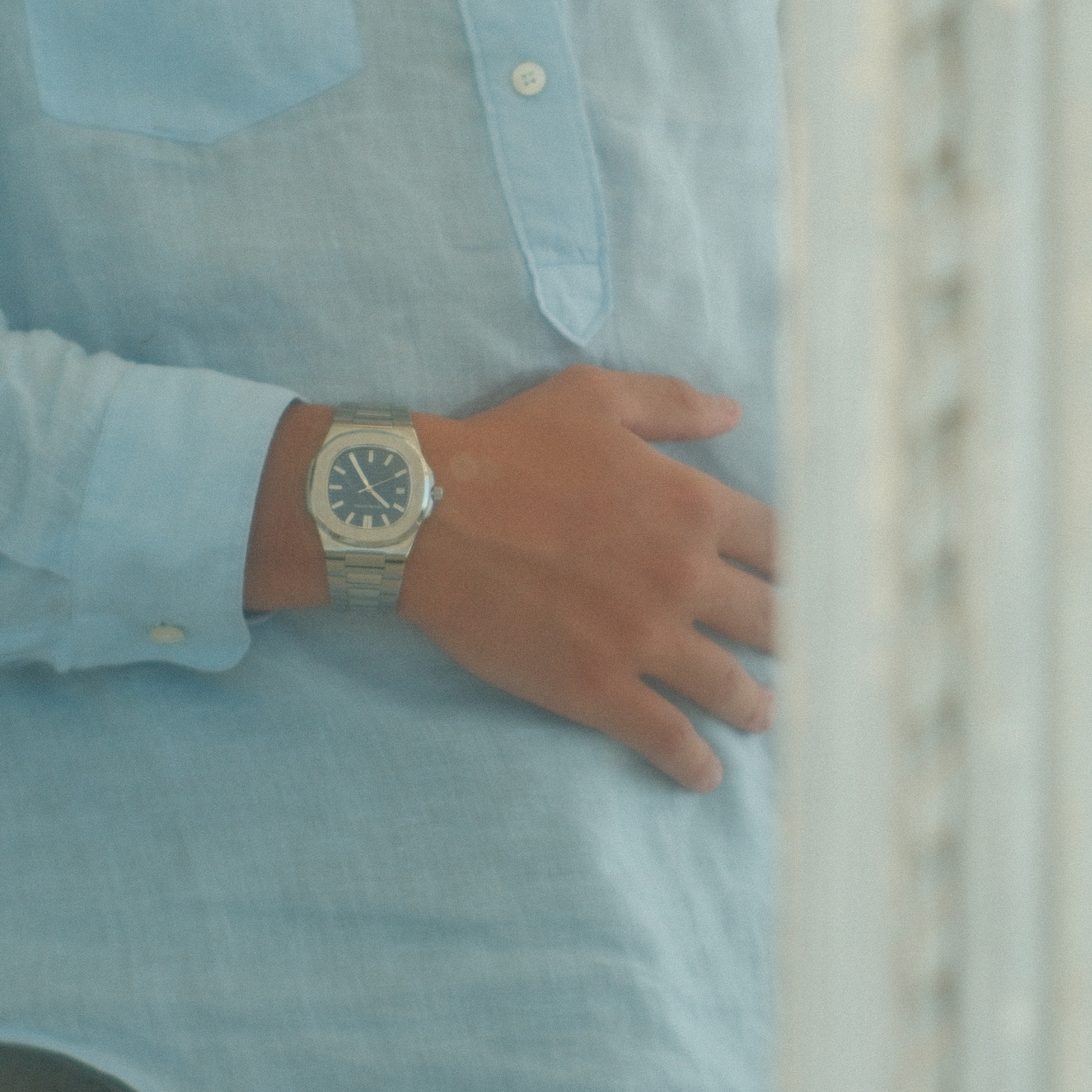 Hand wearing a watch on a light blue shirt with a blurred background